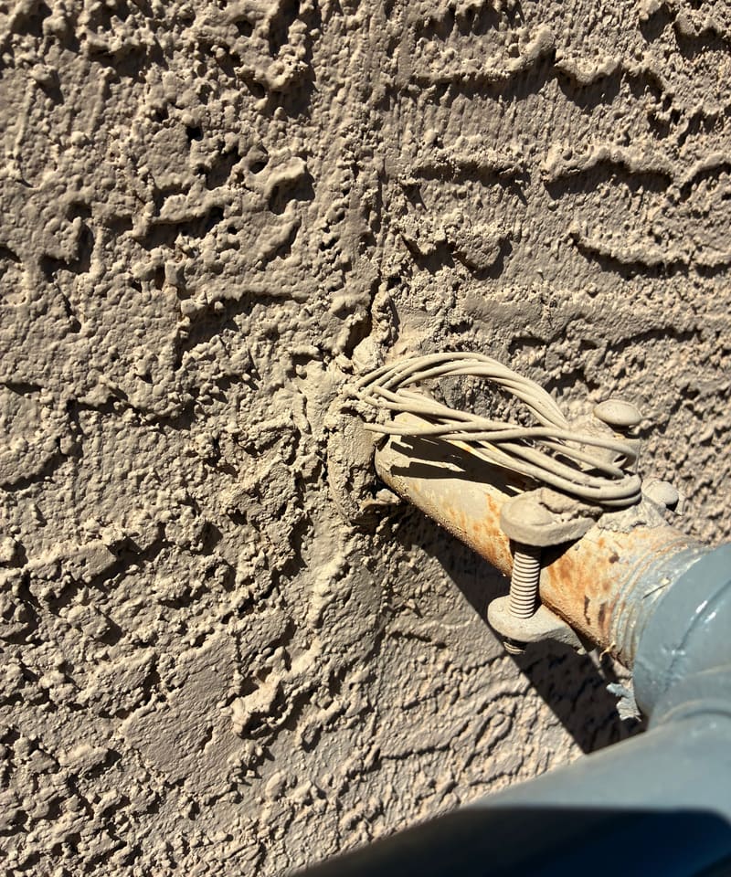 Wiring bundle and pipe entering a stucco wall, with an unsealed gap around it.