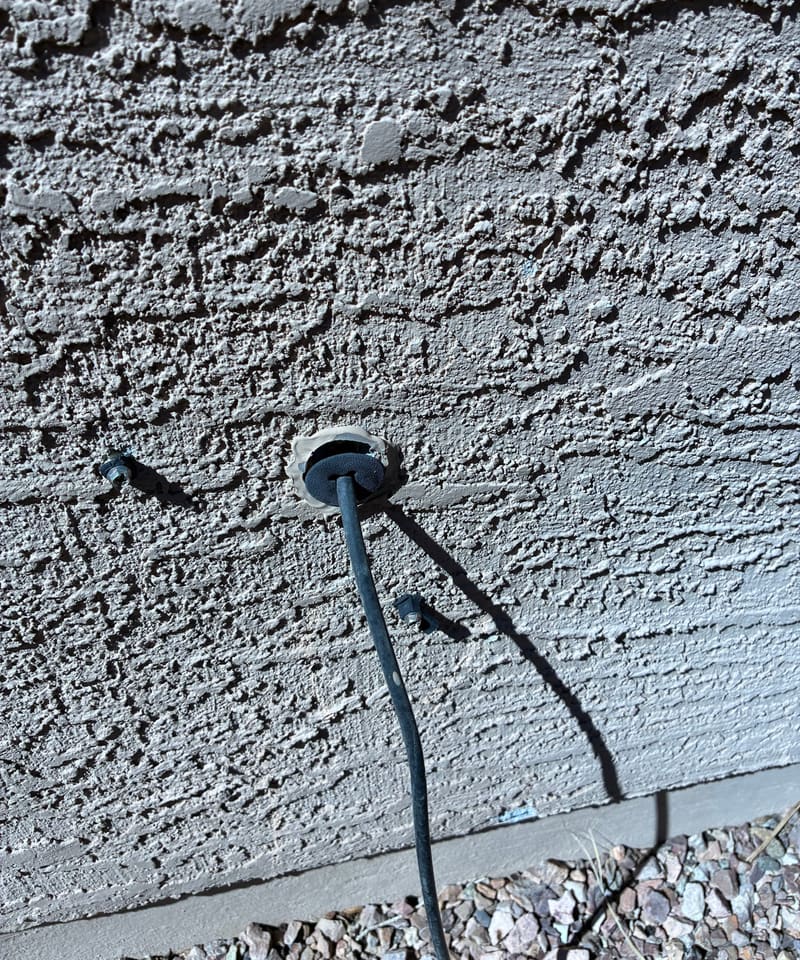 Cable passing through a stucco wall near the ground, a gap that needs sealing.